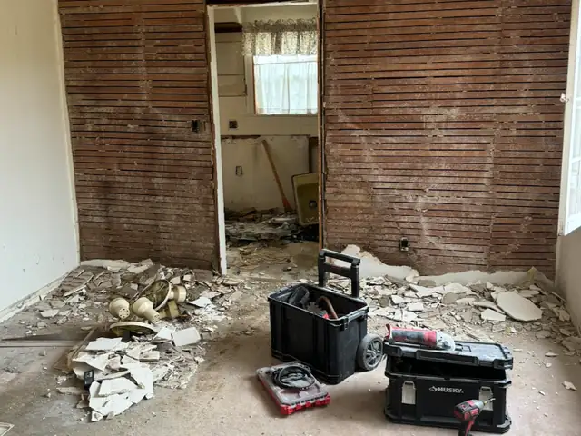 Room with plaster removed from a wall and debris on the floor