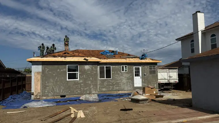 Crew tearing off the old roof on a stucco house, with the roof deck exposed