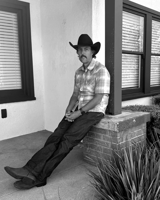 Shawn, owner of Lighthouse Cleanup and Demolition Services, sitting on a brick ledge in a cowboy hat